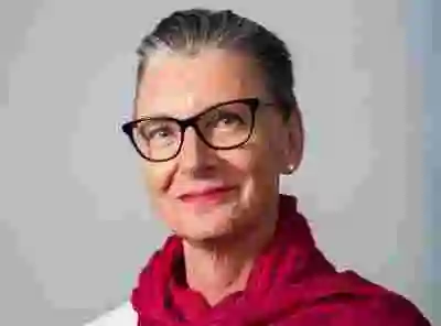 Färgfoto av Konstnärsnämndens direktör Anna Söderbäck med glasögon och röd sjal mot grå bakgrund