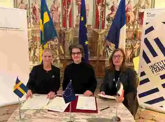 Färgbild på trre kvinnor som sitter vid ett bord och signerar ett dokument.