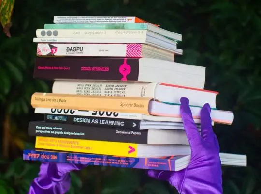 Pilo of books held by hands in purple gloves