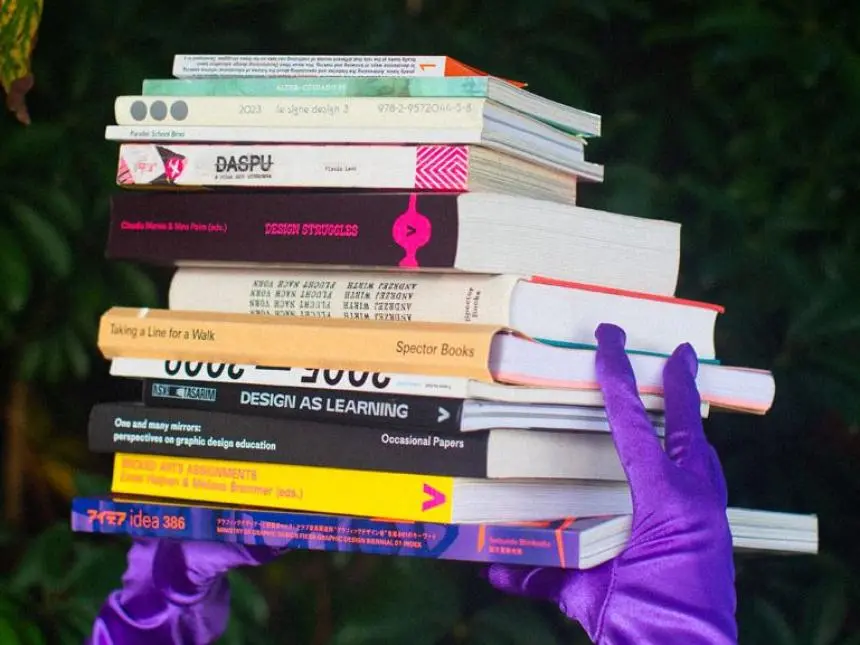 En trave böcker som hålls av händer i lila handskar