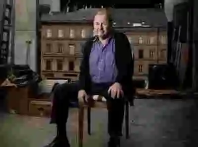 Roy Andersson sitter på en stol framför en filmkuliss