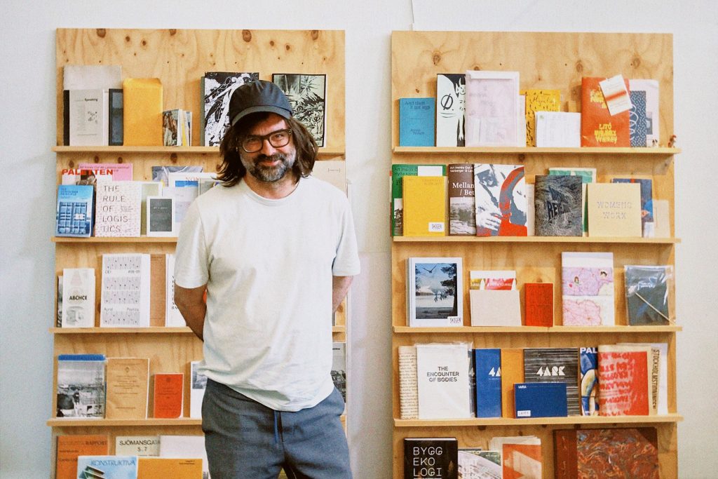 Johan står framför en bokhylla fylld med färgglada böcker