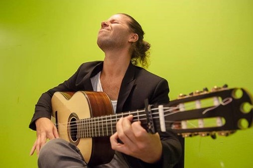 Musikkonstären Robert Svärd spelar guitar framför en grön bakgrund.