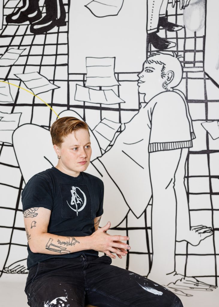 Porträtt av konstnären framför en vägg med konstverk i svartvitt