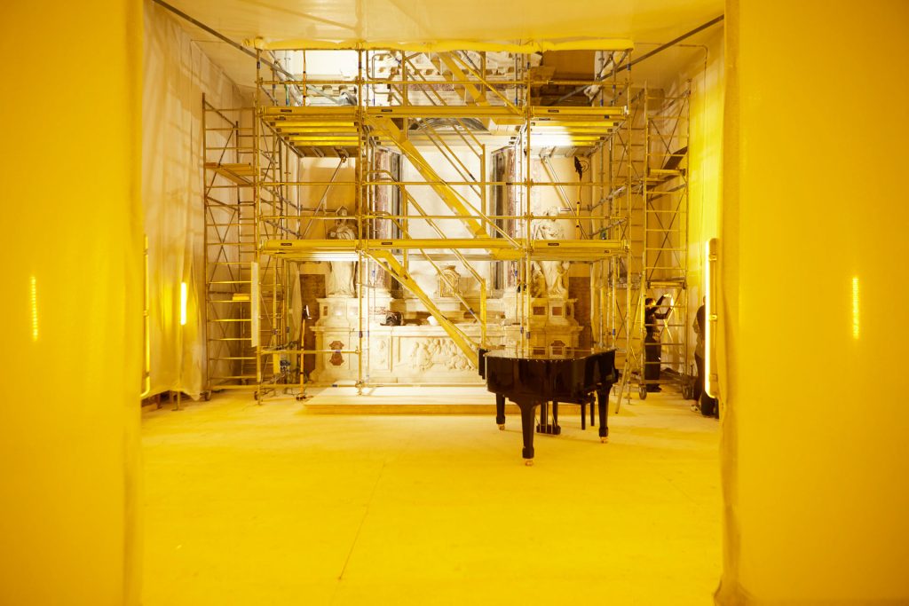 Room in yellow light, with scaffolding and grand piano